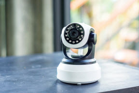 Wireless security camera sitting on table with a window and curtain in the background